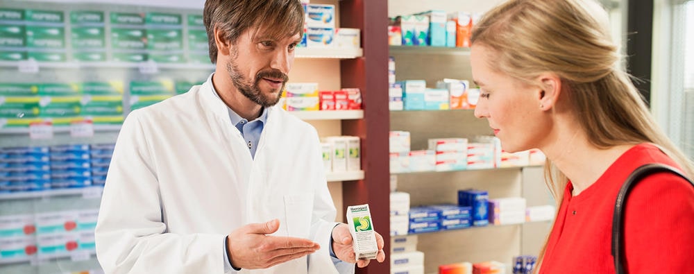 Woman in red sweater buying Iberogast from male salesperson at the pharmacy.