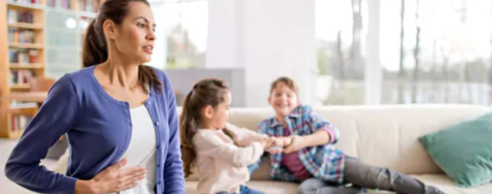 A woman, whose kids are playing in the backgroun, suffering from flatulence.