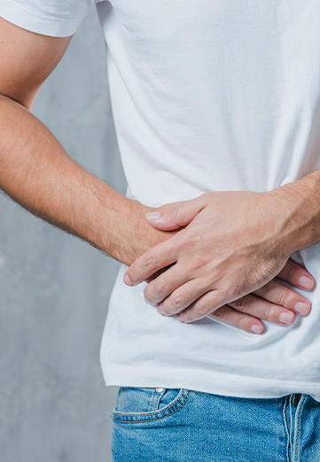 Un hombre vestido con una camiseta blanca, visto solo desde la cadera hasta el hombro, que sufre dolor estomacal